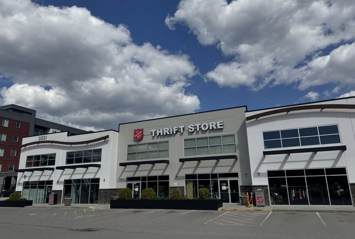 Exterior view of a Salvation Army thrift store building with large windows and signage, set in a shopping plaza under a partly cloudy sky with an empty parking lot in front.