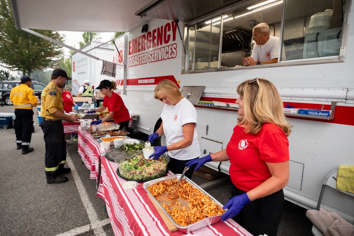 Volunteers serving hot meals from a Salvation Army Emergency Disaster Services truck, with tables set up outdoors holding trays of prepared food.
