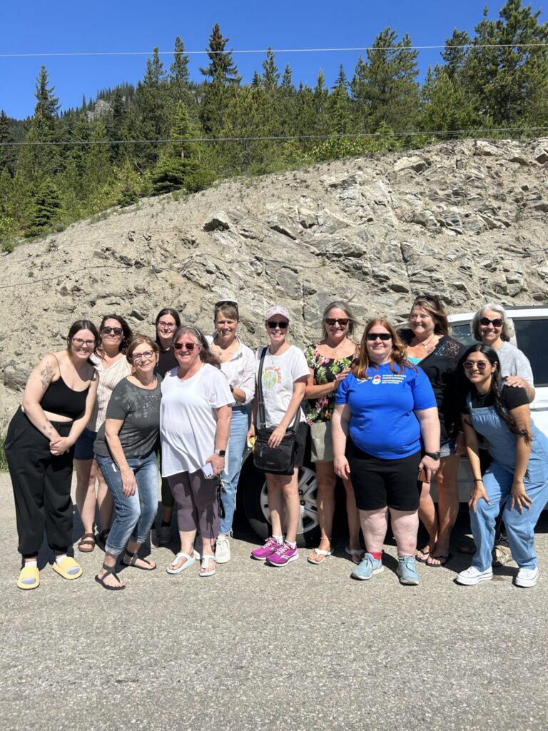 Group of women standing together outdoors in front of a rocky hillside, posing for a photo during a womens ministry gathering.